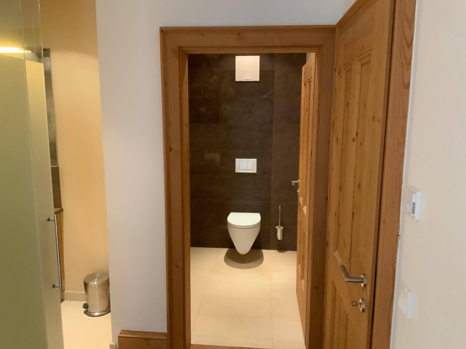 Modernes WC mit wandhängender Toilette und dunklen Fliesen an der Wand.