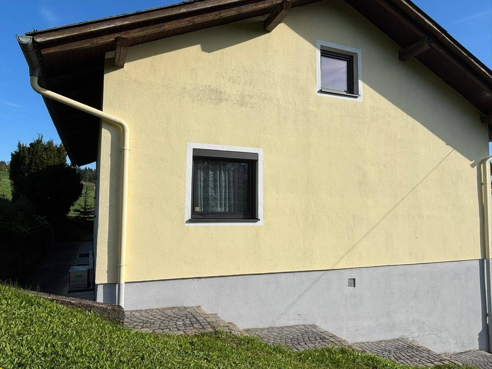 Nahaufnahme der gelben Hausfassade mit einem Fenster und Rollladen sowie einer Steintreppe.