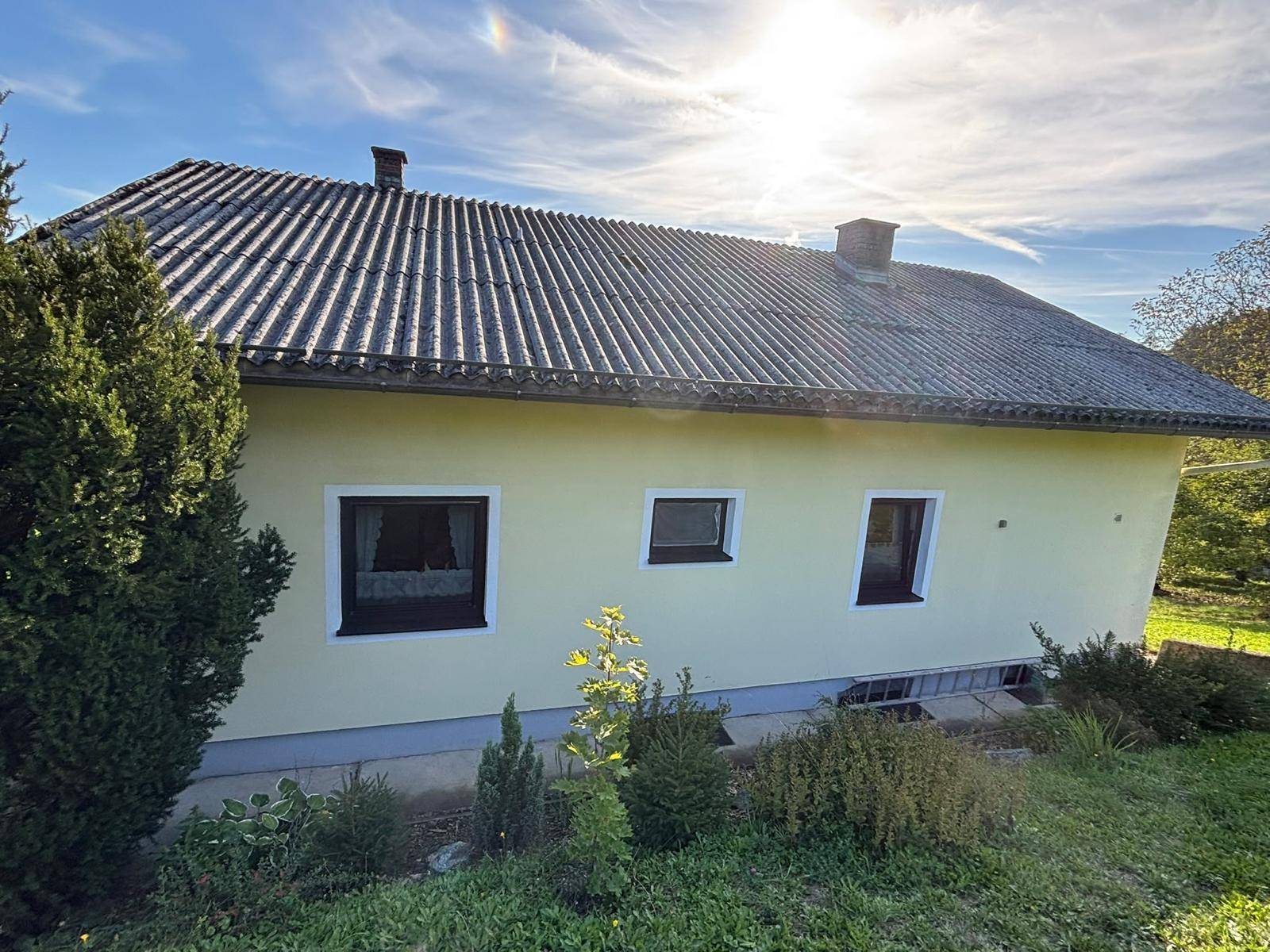 Rückseite des Hauses mit gelber Fassade, mehreren Fenstern und einem Satteldach unter sonnigem Himmel.