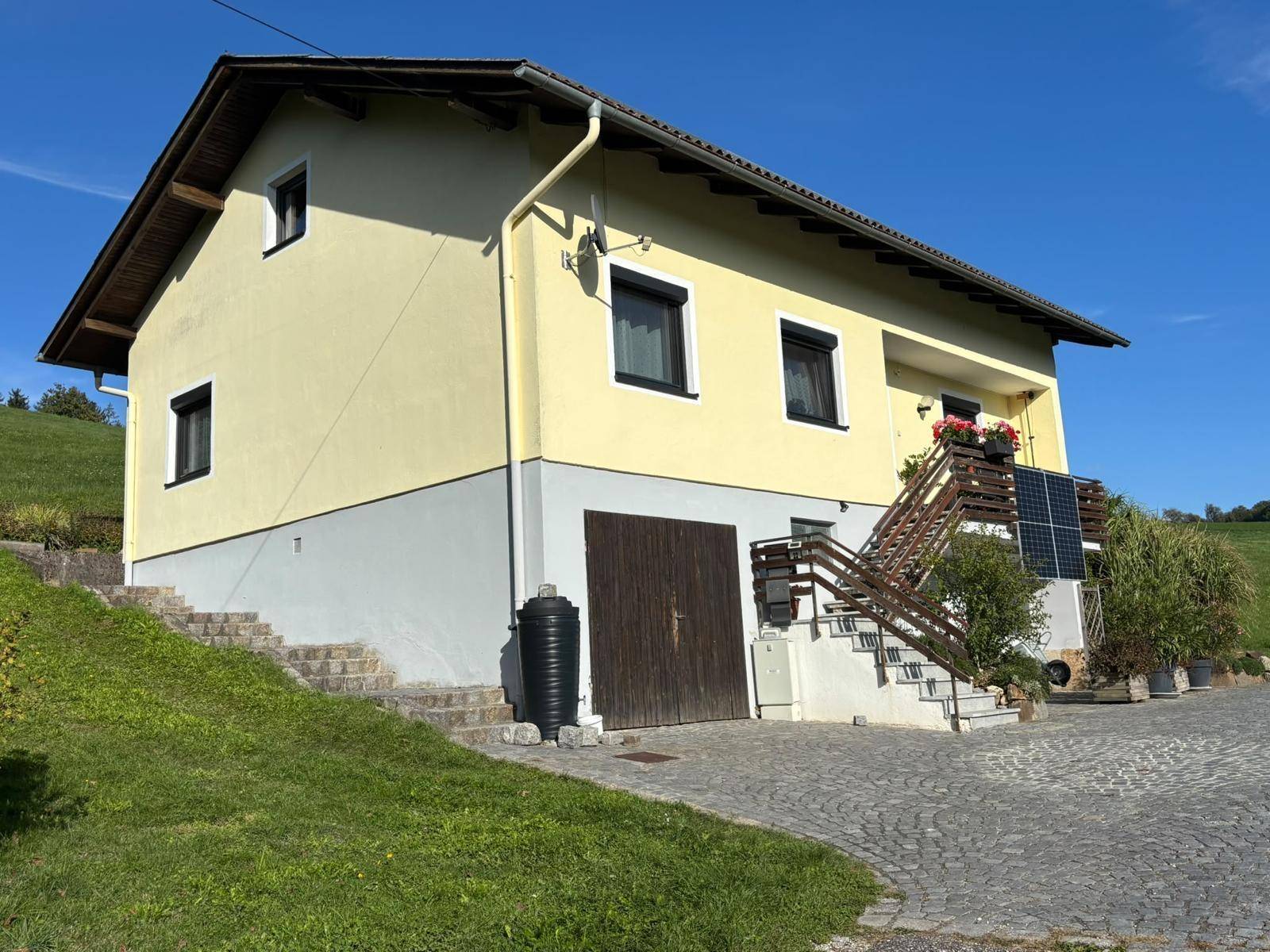 Seitenansicht des Hauses mit gelber Fassade, Garage und Außentreppe zum Eingangsbereich.