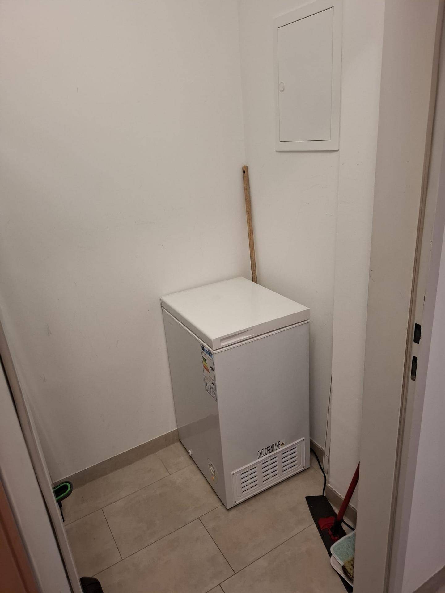Kleiner Abstellraum mit Gefrierschrank und Fliesenboden.