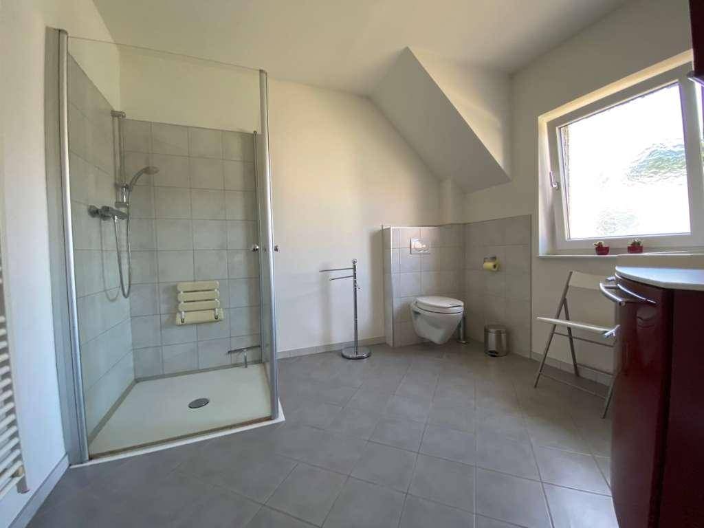 Geräumiges Badezimmer mit ebenerdiger Dusche, Toilette und Fenster unter Dachschräge.