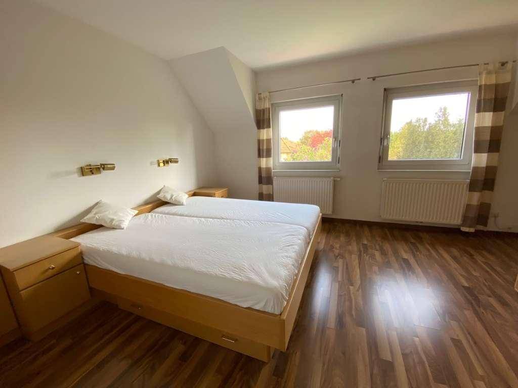Gemütliches Schlafzimmer mit Doppelbett, Laminatboden und zwei Fenstern unter Dachschräge.