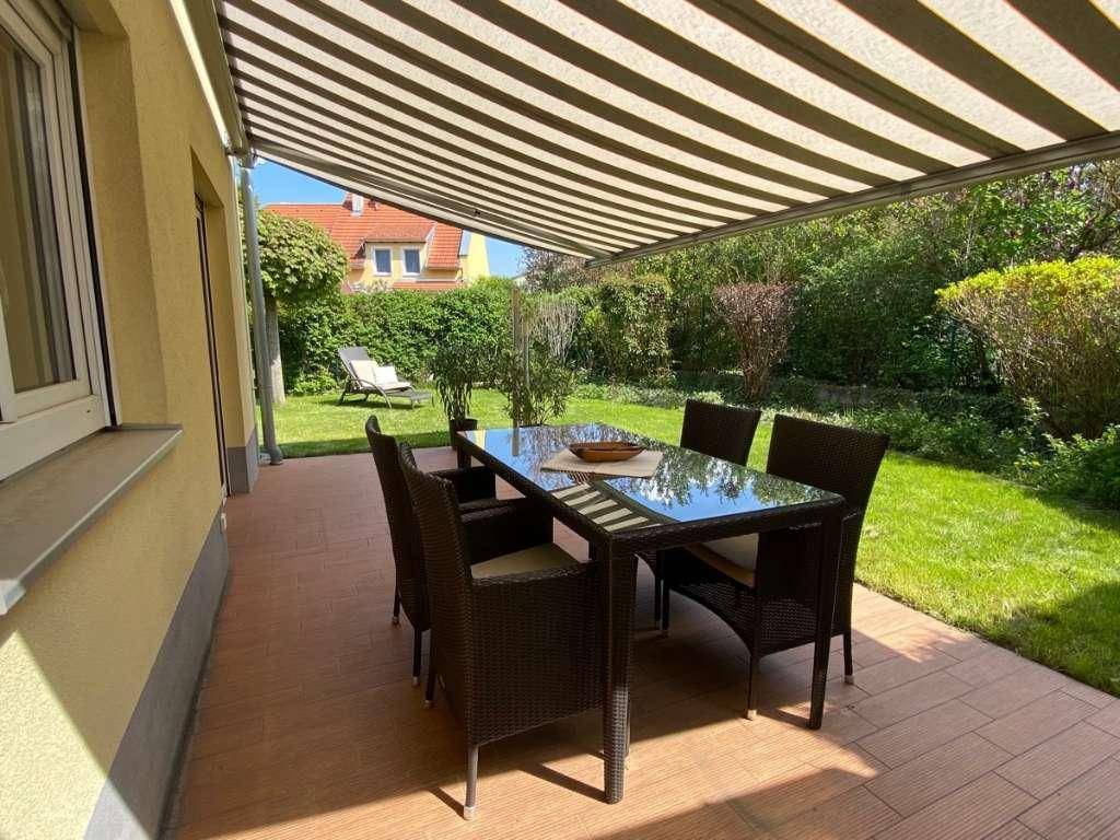 Gemütliche Terrasse mit Esstisch, Stühlen und ausziehbarer Markise, umgeben von Grün.