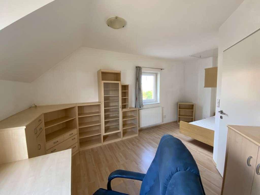 Helles Zimmer unter der Dachschräge mit Laminatboden und viel Stauraum durch Regale.