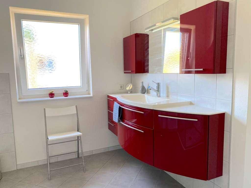 Modernes Badezimmer mit roten Hochglanzmöbeln, Waschbecken und einem Fenster.