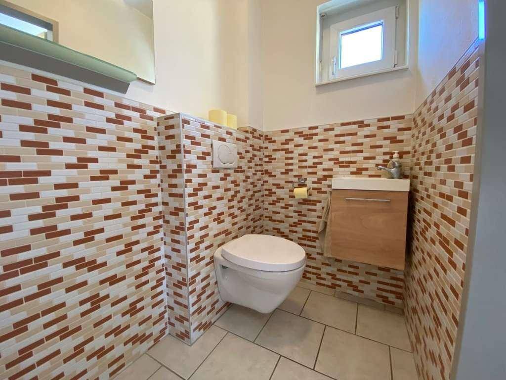 Modernes Gäste-WC mit dekorativen Fliesen, wandhängender Toilette und kleinem Waschbecken.