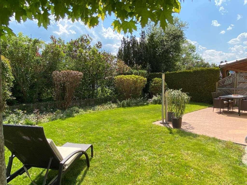 Blick in den grünen Garten mit Rasen, Sonnenliege und einer Terrasse im Hintergrund.