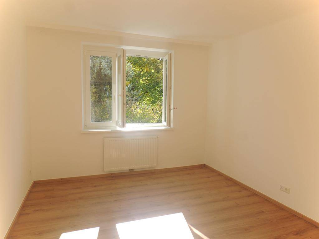 Helles Schlafzimmer mit geöffnetem Fenster, das frische Luft und einen schönen Grünblick bietet.