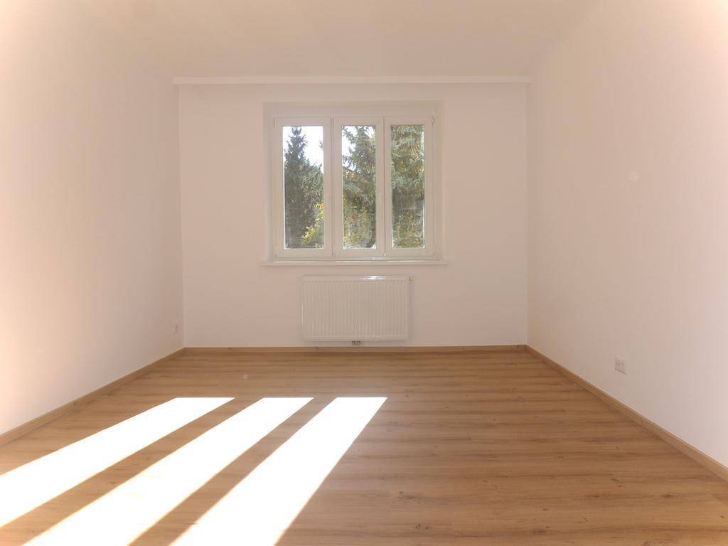 Geräumiges Schlafzimmer mit hellem Laminatboden und großem Fenster mit Blick ins Grüne.