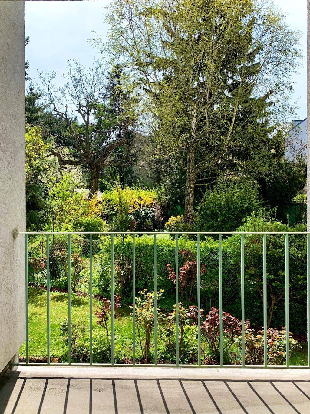 Balkon mit Blick auf einen gepflegten Garten mit vielen Bäumen und Sträuchern.