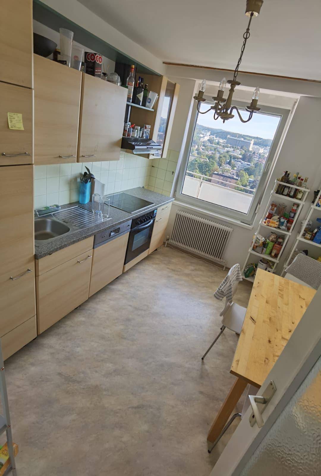 Funktionale Küche mit hellen Holzschränken, Essbereich und Fenster mit Stadtblick.