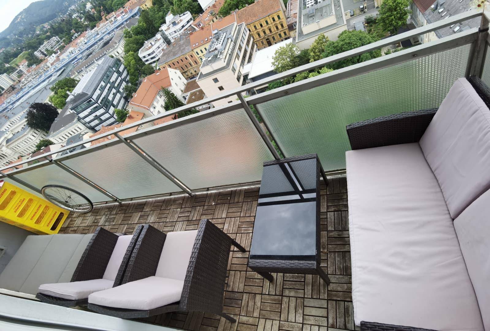 Möblierter Balkon mit Rattanmöbeln und Blick auf die umliegenden Gebäude der Stadt.