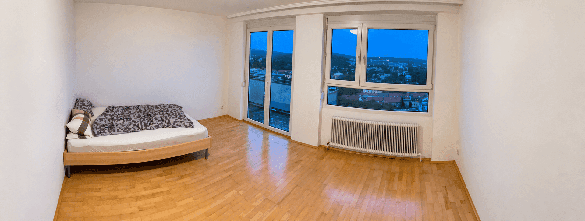 Helles Schlafzimmer mit Holzboden, großem Fenster und Zugang zu einem Balkon mit Flussblick.