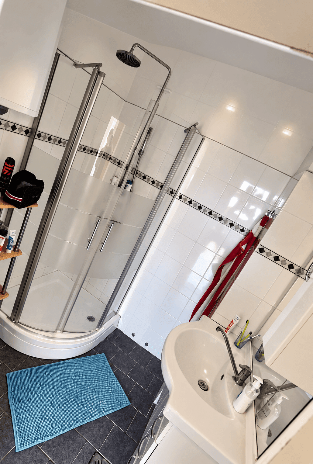 Modernes Badezimmer mit Eckdusche, Waschbecken und weißen Fliesen an den Wänden.