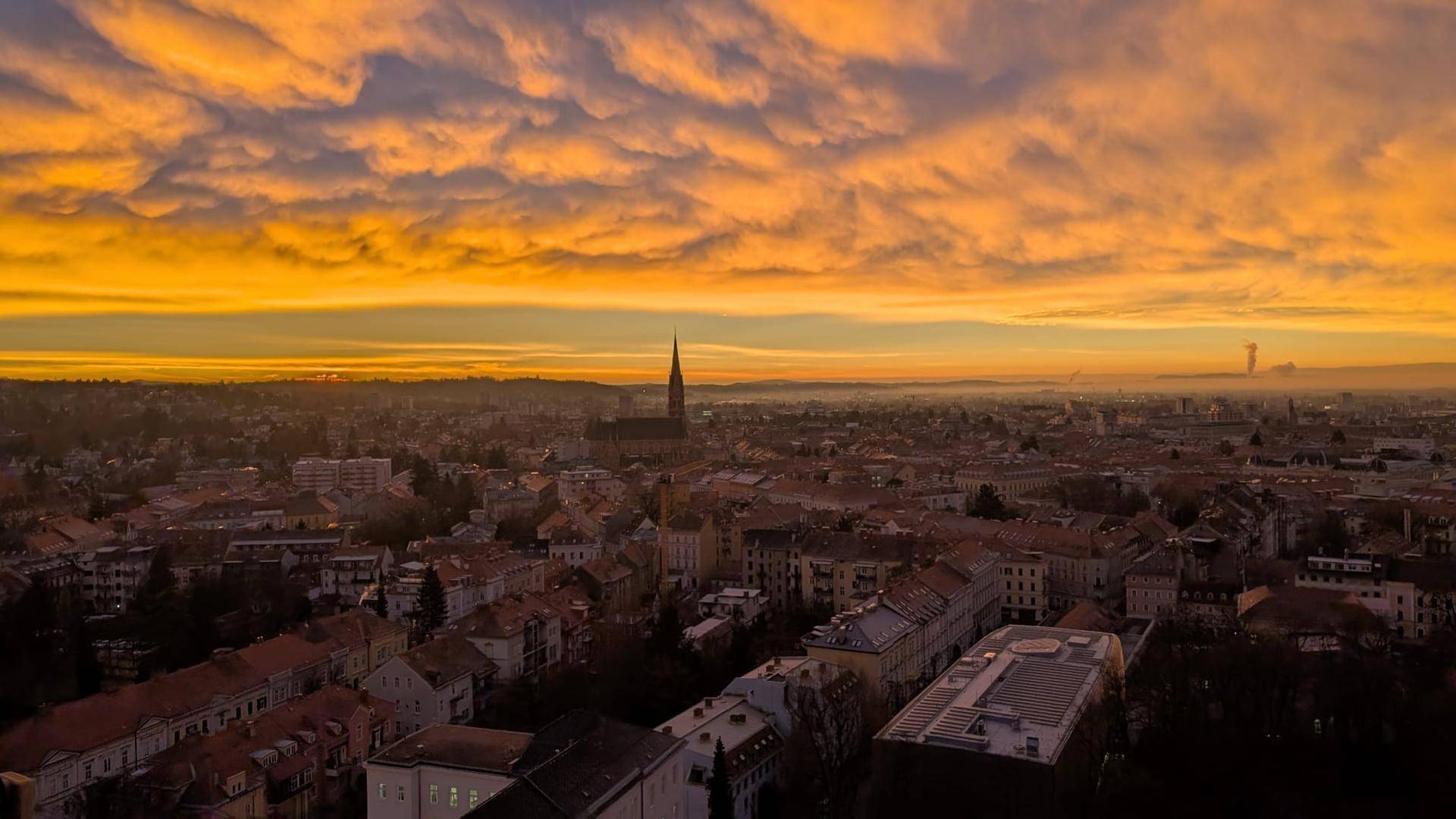 Spektakulärer Sonnenuntergang über der Stadt mit leuchtend orangefarbenen Wolken am Himmel.