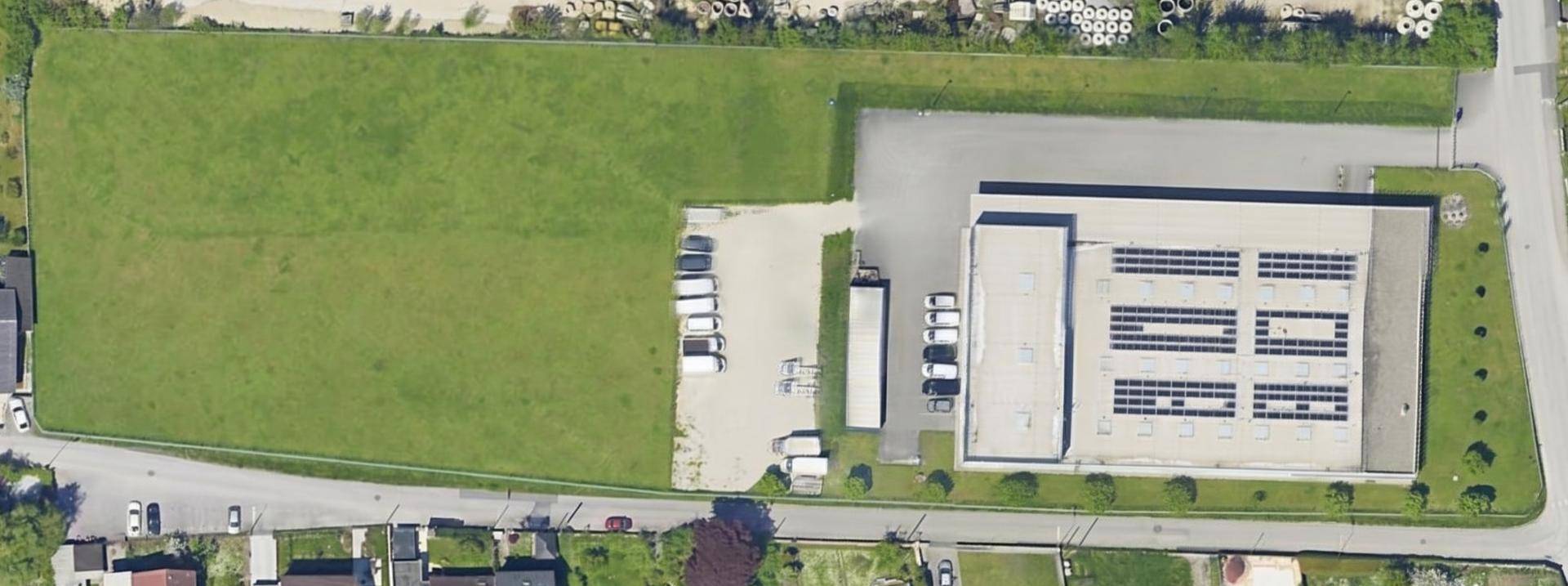 Luftaufnahme eines großen Grundstücks mit Grünfläche, Gebäude mit Solaranlage und Parkplätzen.