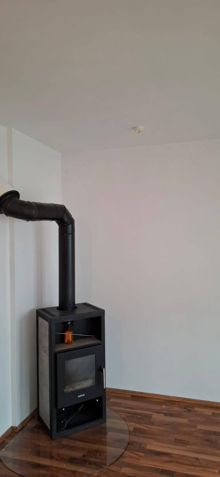 Heller Raum mit Holzboden und einem modernen Holzofen für gemütliche Abende.