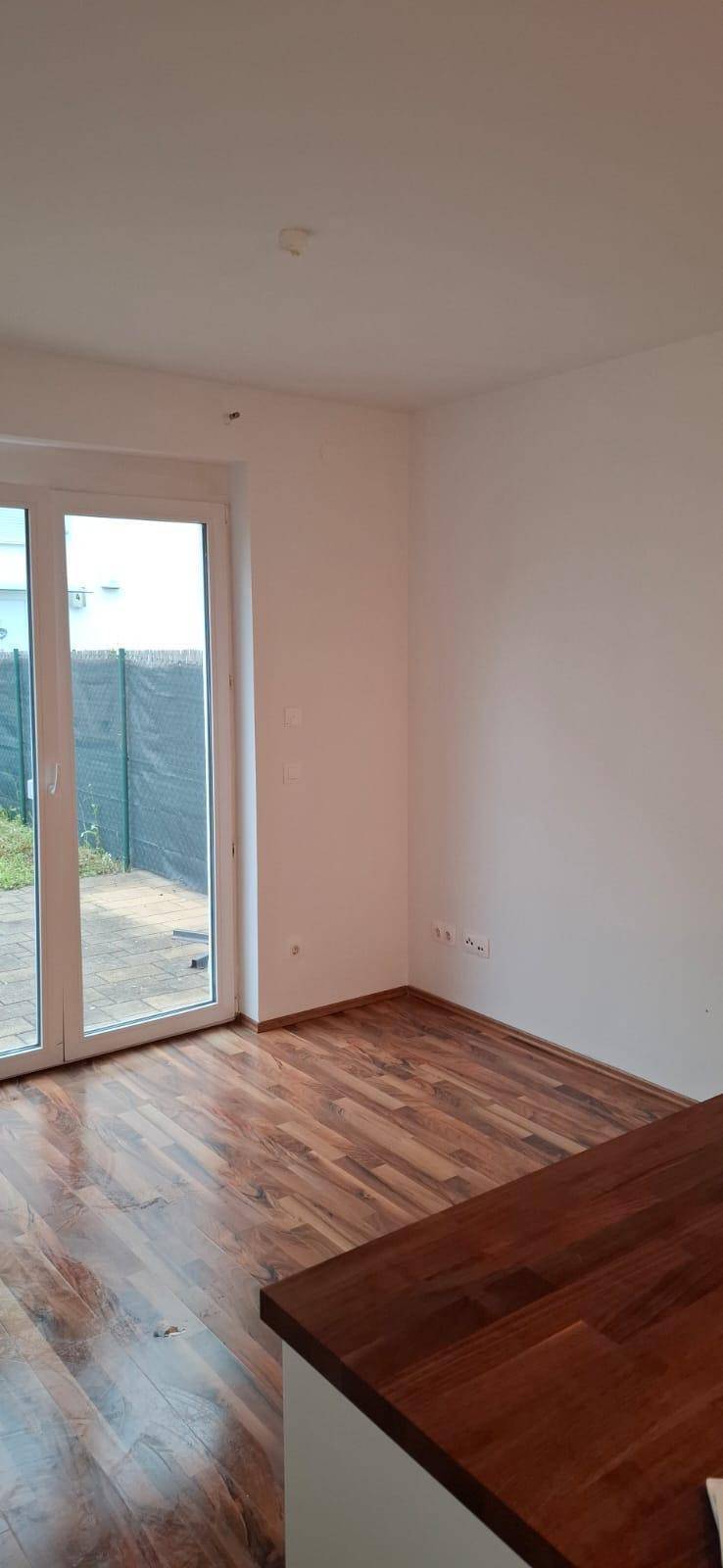 Heller Wohnbereich mit Holzboden und großen Fenstern, angrenzend an die Küche.