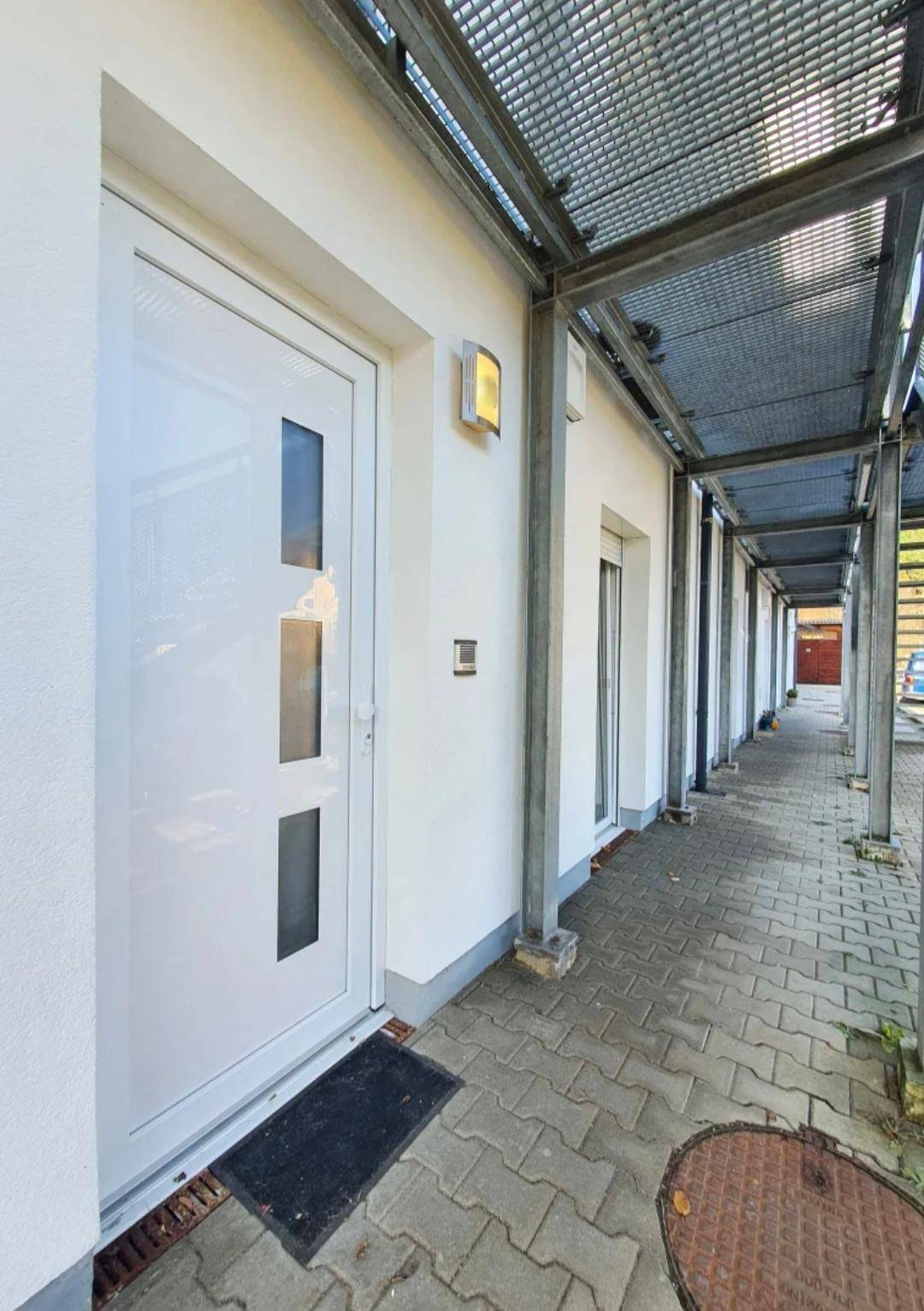 Heller Eingangsbereich mit moderner Tür und überdachtem Zugang.