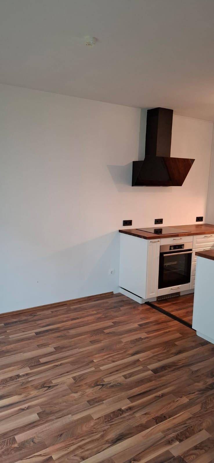 Geräumige Küche mit Holzboden, weißer Einrichtung und moderner Dunstabzugshaube.