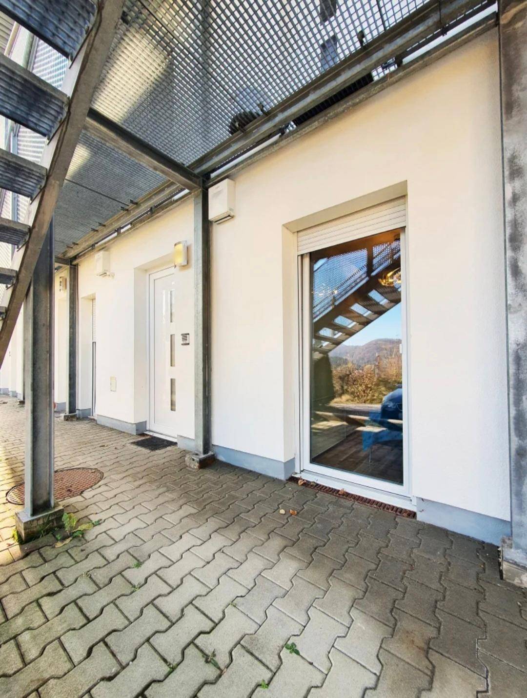 Eingangsbereich eines Gebäudes mit gepflastertem Weg und Außentreppe.