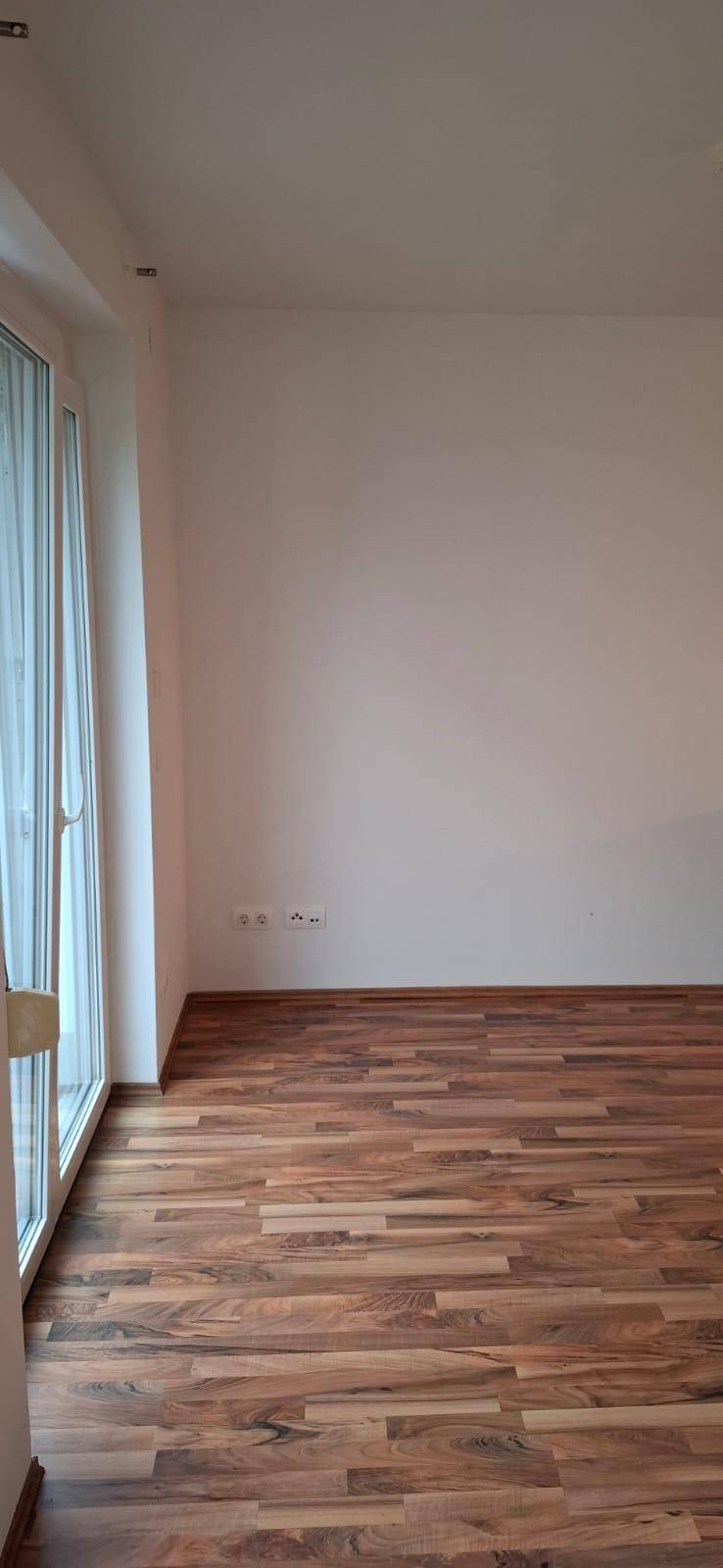 Lichtdurchfluteter Raum mit Holzboden und großen Fenstern, ideal für einen Wohnbereich.