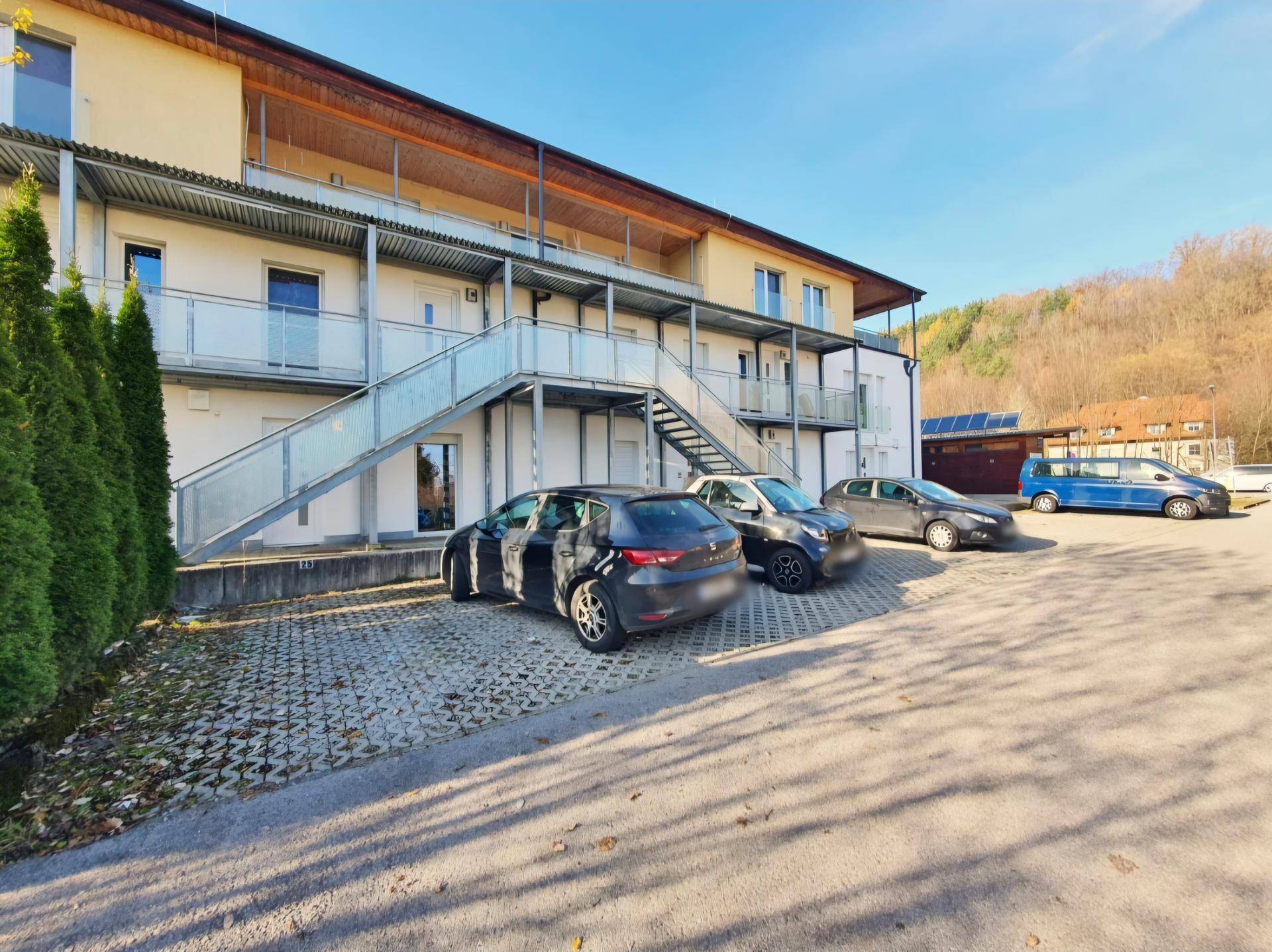 Außenansicht des Gebäudes mit Parkplätzen und Zugang über eine Metalltreppe.