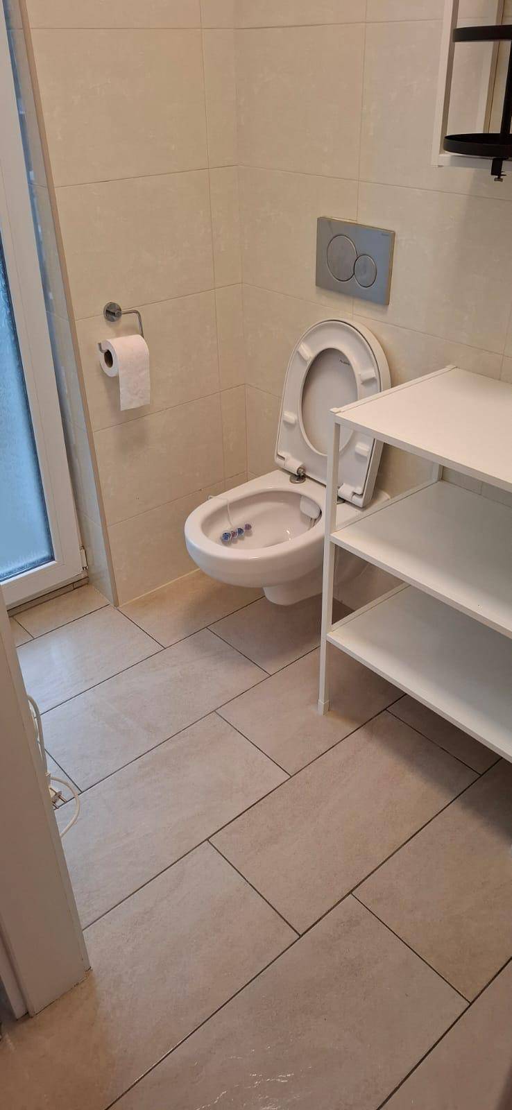 Modernes WC mit Wand-WC, Bidetfunktion und hellen Fliesen.