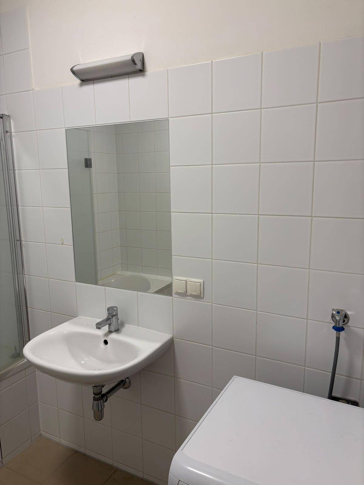 Waschbecken mit Spiegel und Waschmaschine im hell gefliesten Badezimmer.