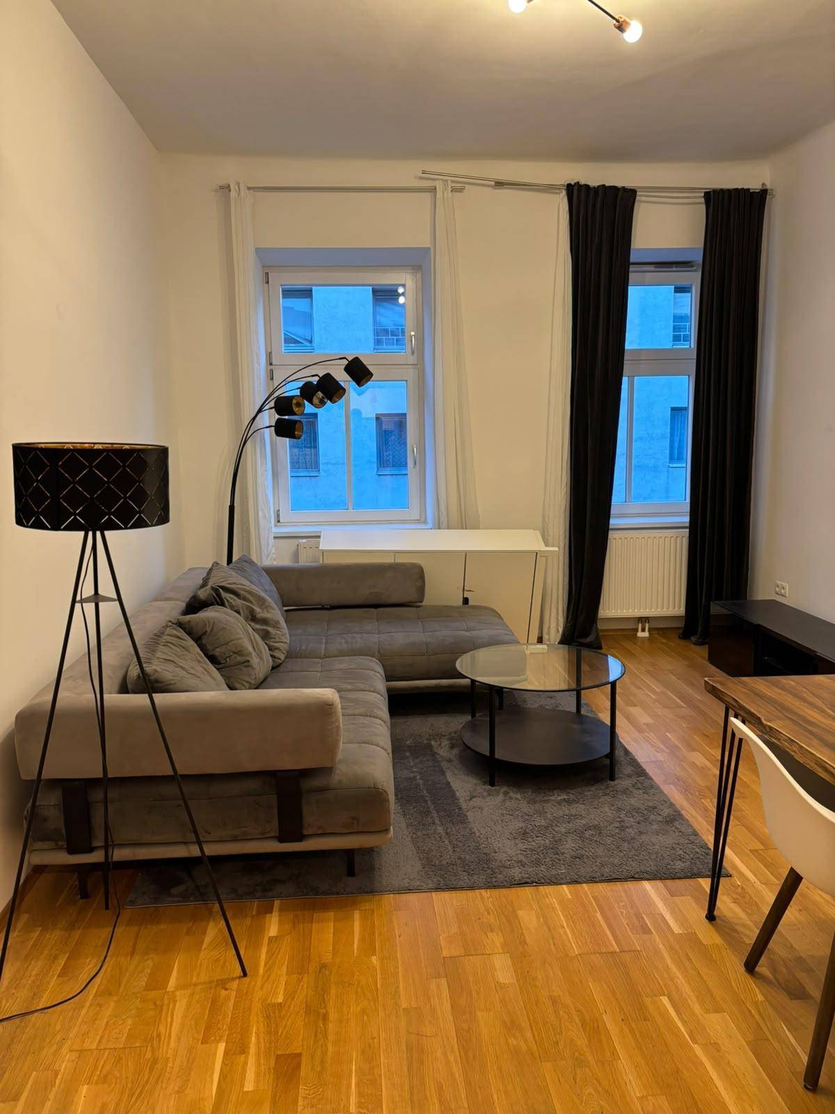 Gemütlicher Wohn- und Essbereich mit grauem Ecksofa, Couchtisch und Holzboden.