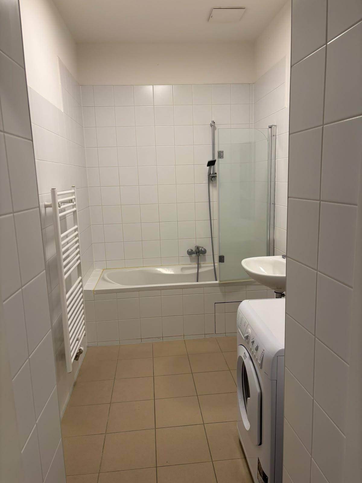 Gefliestes Badezimmer mit Badewanne, Duschabtrennung, Waschbecken und Waschmaschine.