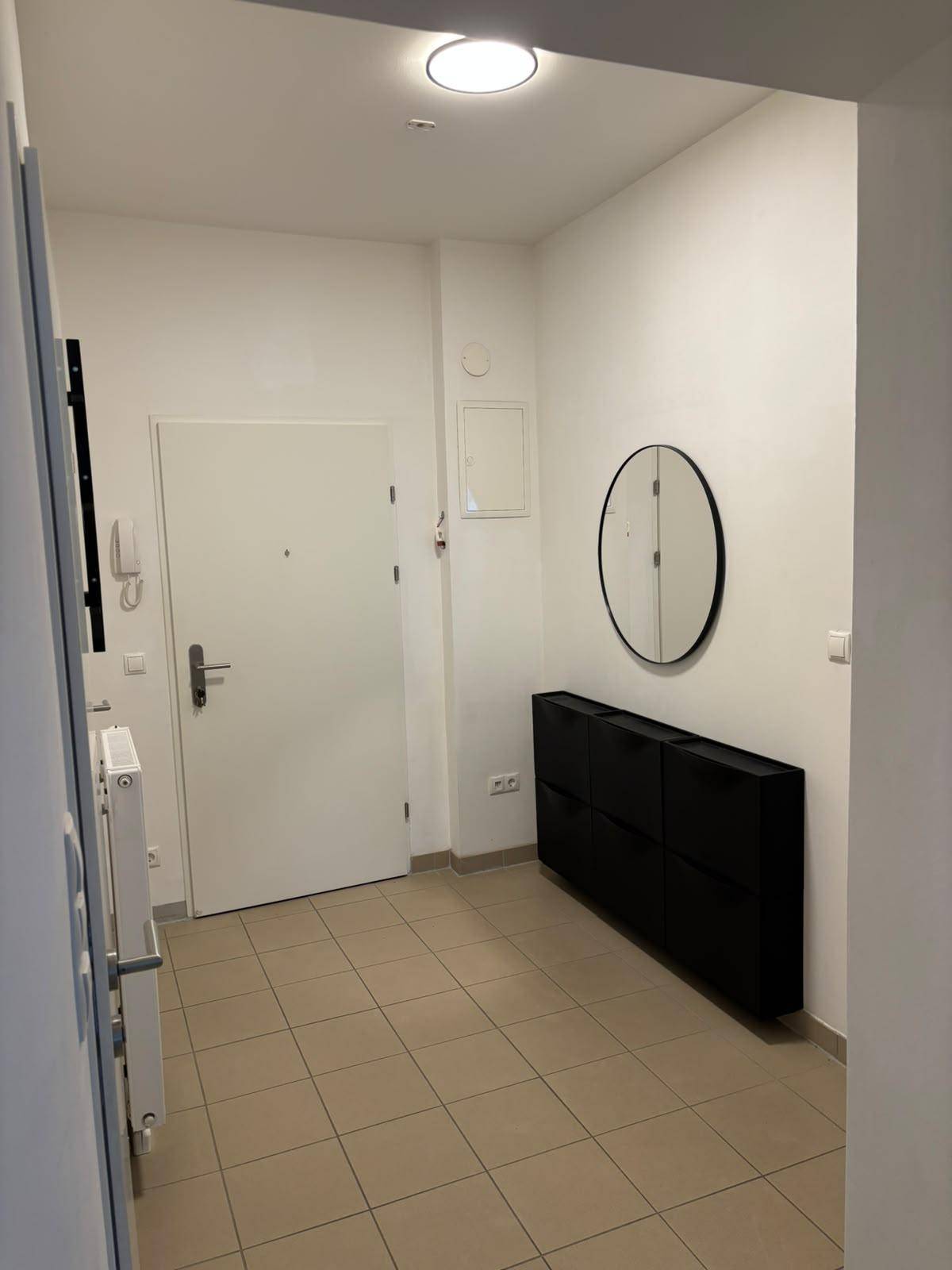 Eingangsbereich mit Fliesenboden, einem Schuhschrank und einem runden Wandspiegel.