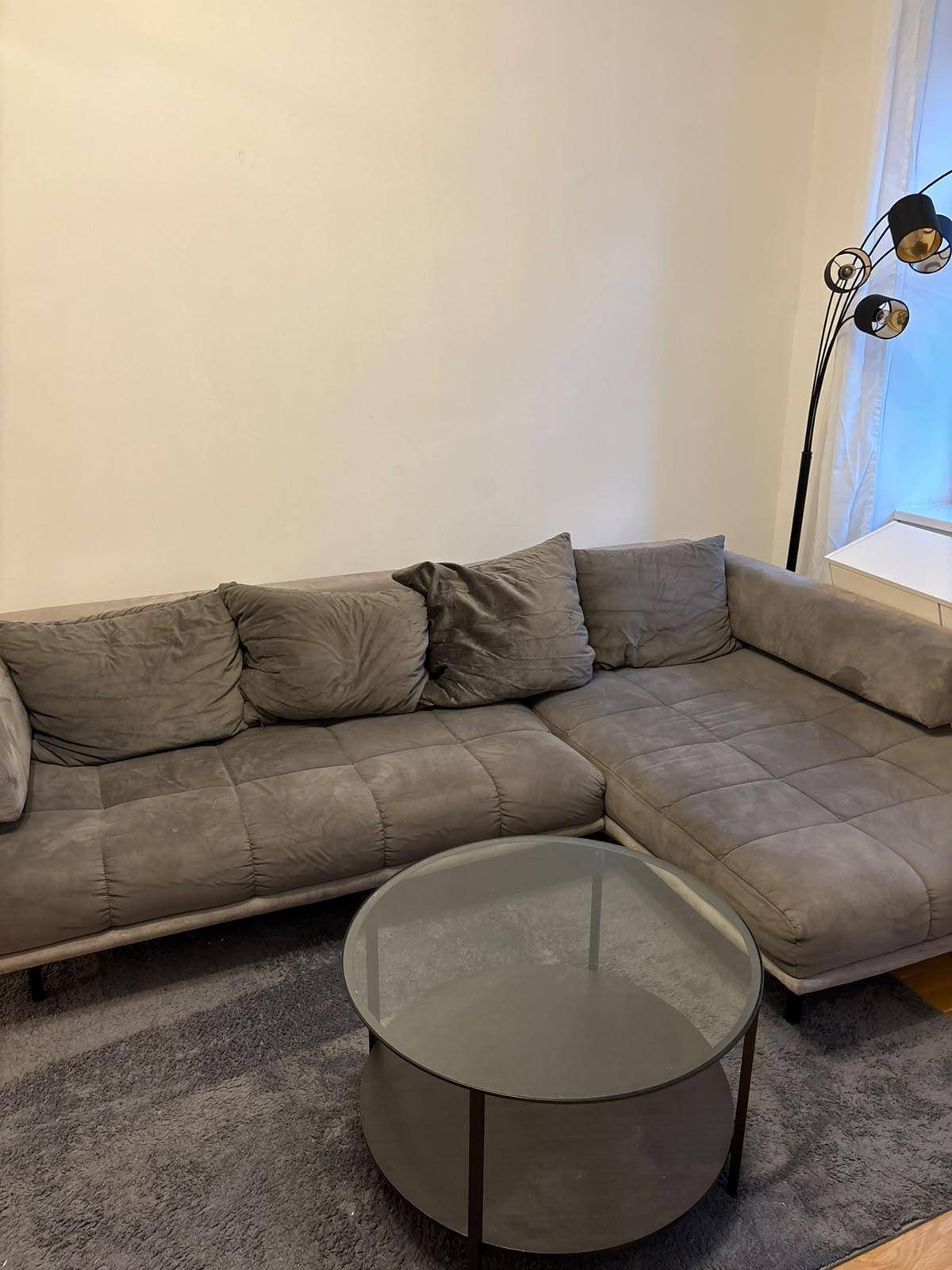 Detailansicht des bequemen grauen Ecksofas und des runden Glastisches im Wohnzimmer.