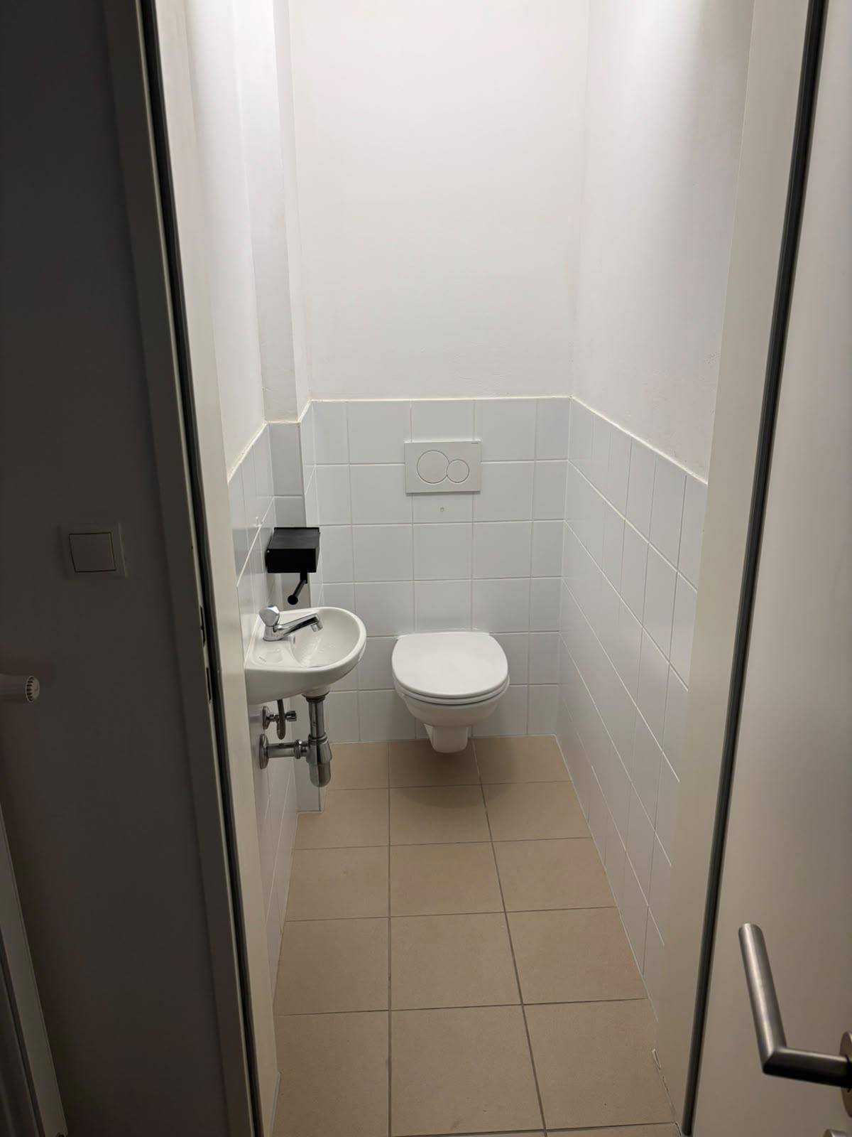 Separates Gäste-WC mit wandhängender Toilette und kleinem Handwaschbecken.