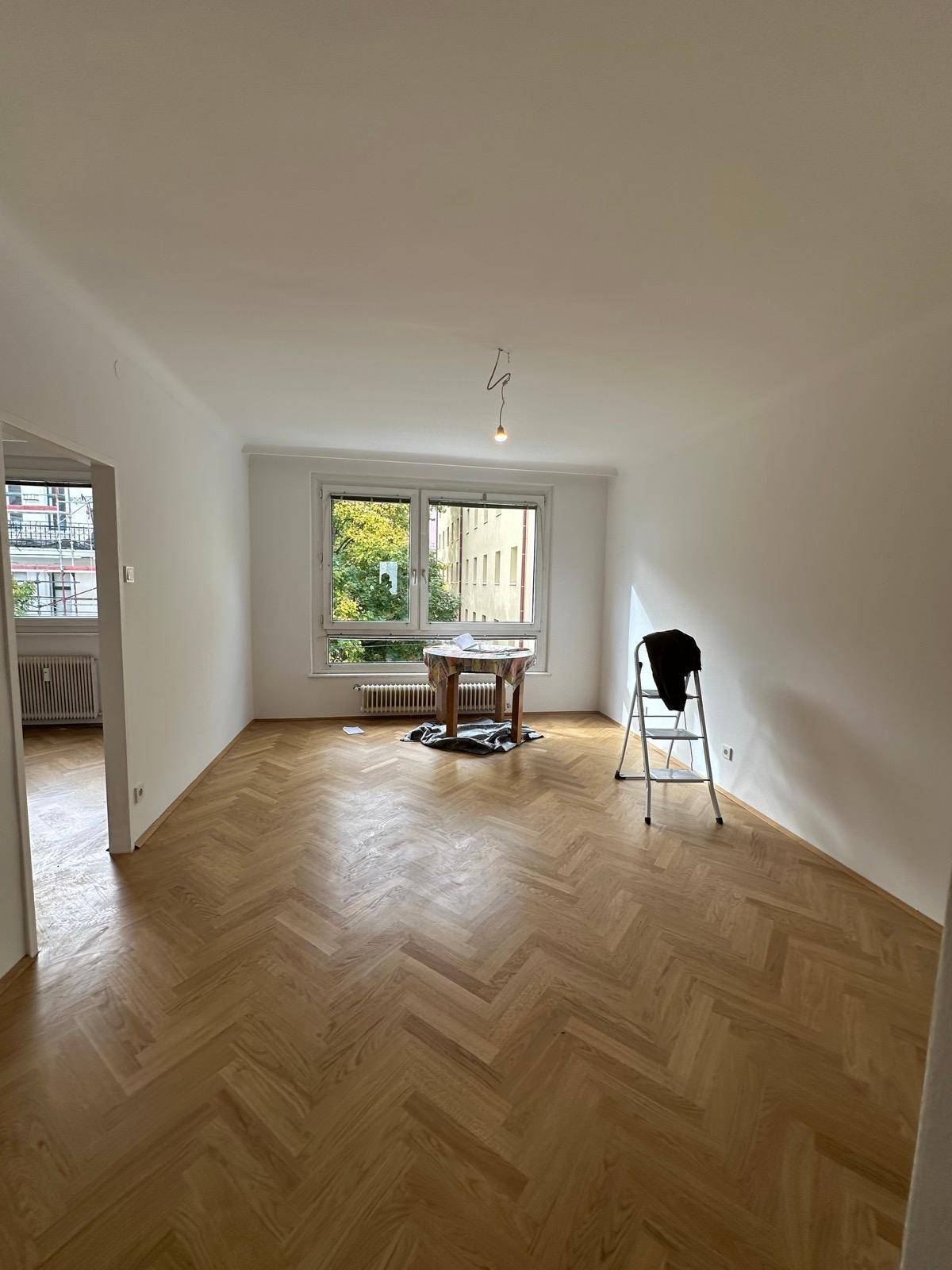 Großes, helles Wohnzimmer mit Fischgrätparkett und breiten Fenstern, die viel Licht spenden und Grünblick bieten.