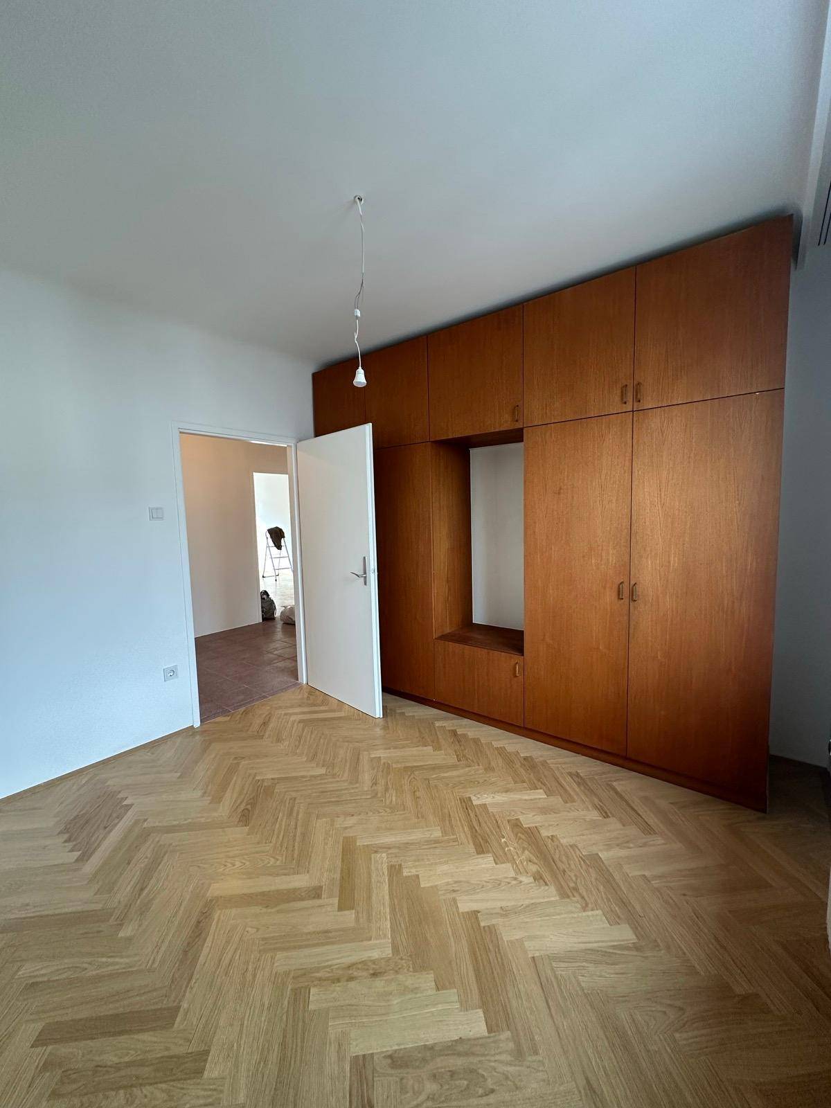 Geräumiges Schlafzimmer mit elegantem Fischgrätparkett und einem großen, integrierten Holzschrank an der Wand.
