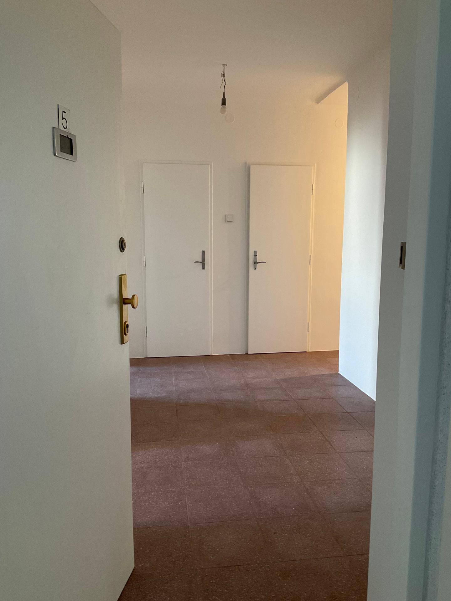 Heller Eingangsbereich einer Wohnung mit braunen Fliesen und weißen Türen, die zu weiteren Räumen führen.