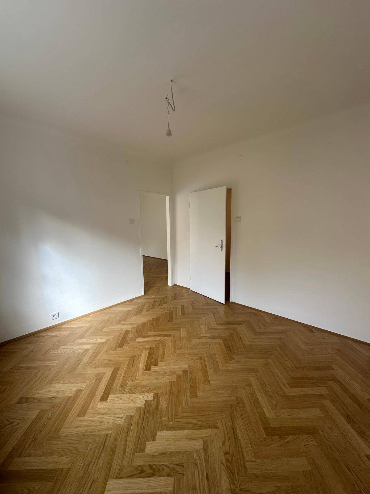 Geräumiges Zimmer mit elegantem Fischgrätparkett und weiß gestrichenen Wänden, bereit zur individuellen Einrichtung.