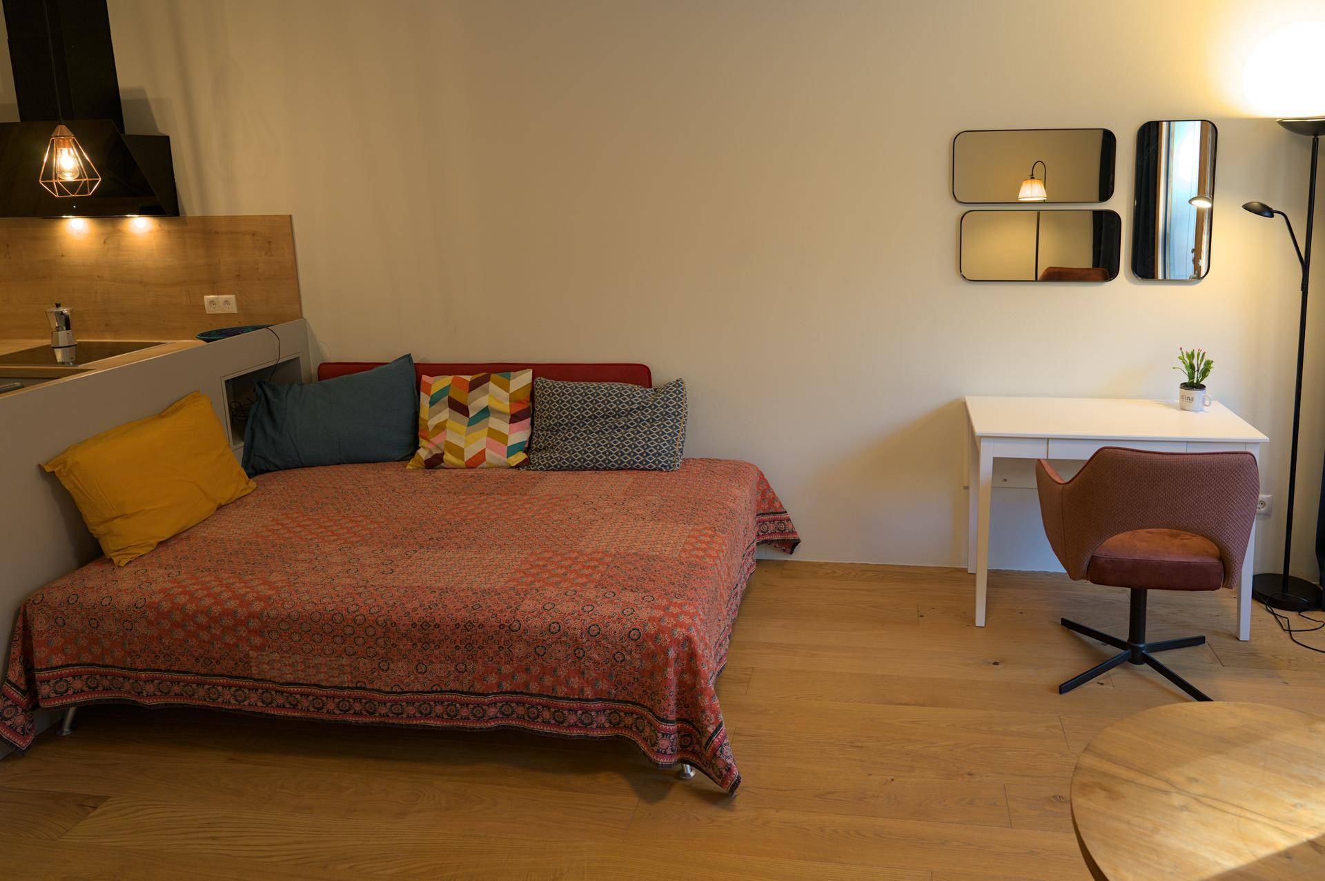 Gemütlicher Wohnbereich mit Schlafsofa, kleinem Tisch und integrierter Küchenzeile im Hintergrund.