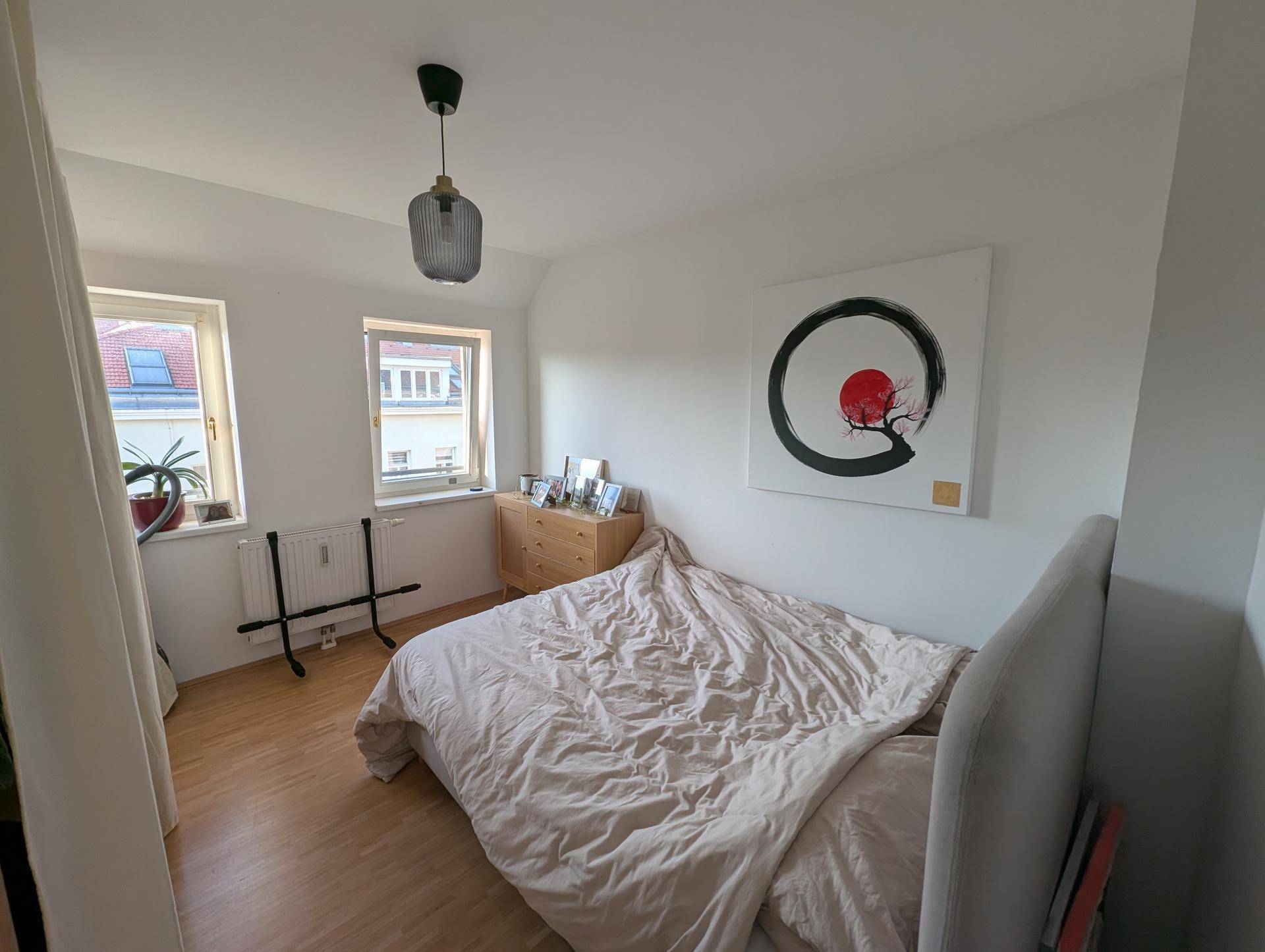 Helles Schlafzimmer mit Doppelbett, Holzkommode und Kunstwerk an der Wand.