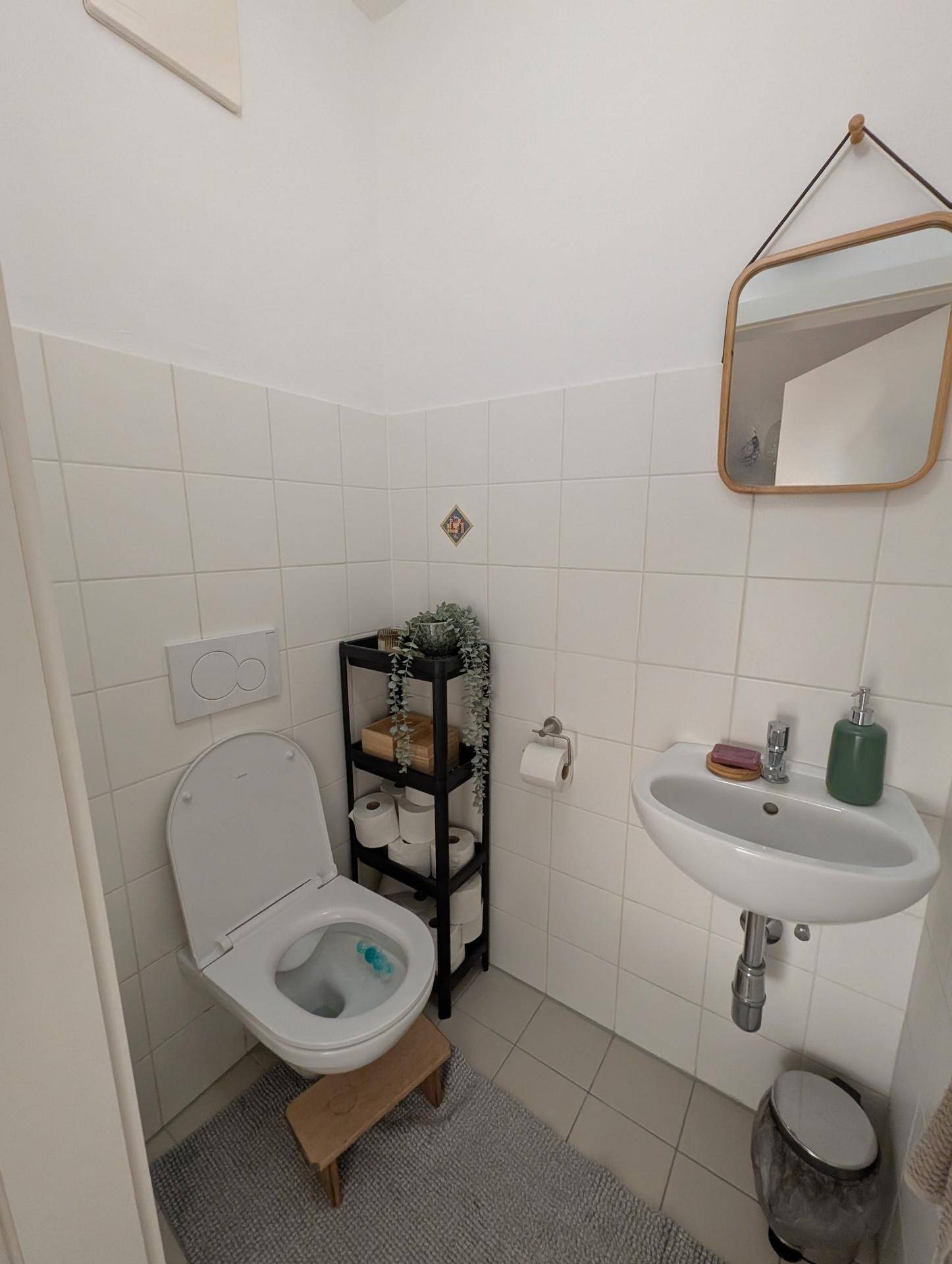 Kleines Gäste-WC mit Wand-WC, Waschbecken und Spiegel, hell gefliest.