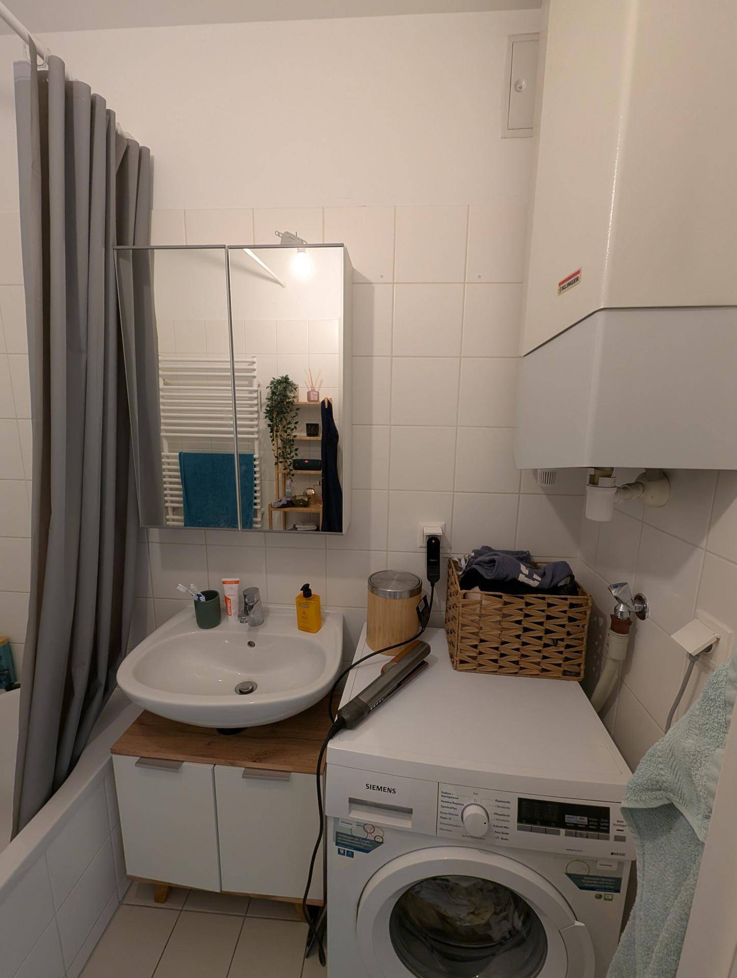 Badezimmer mit Waschmaschine, Waschbecken und Spiegelschrank über der Badewanne.