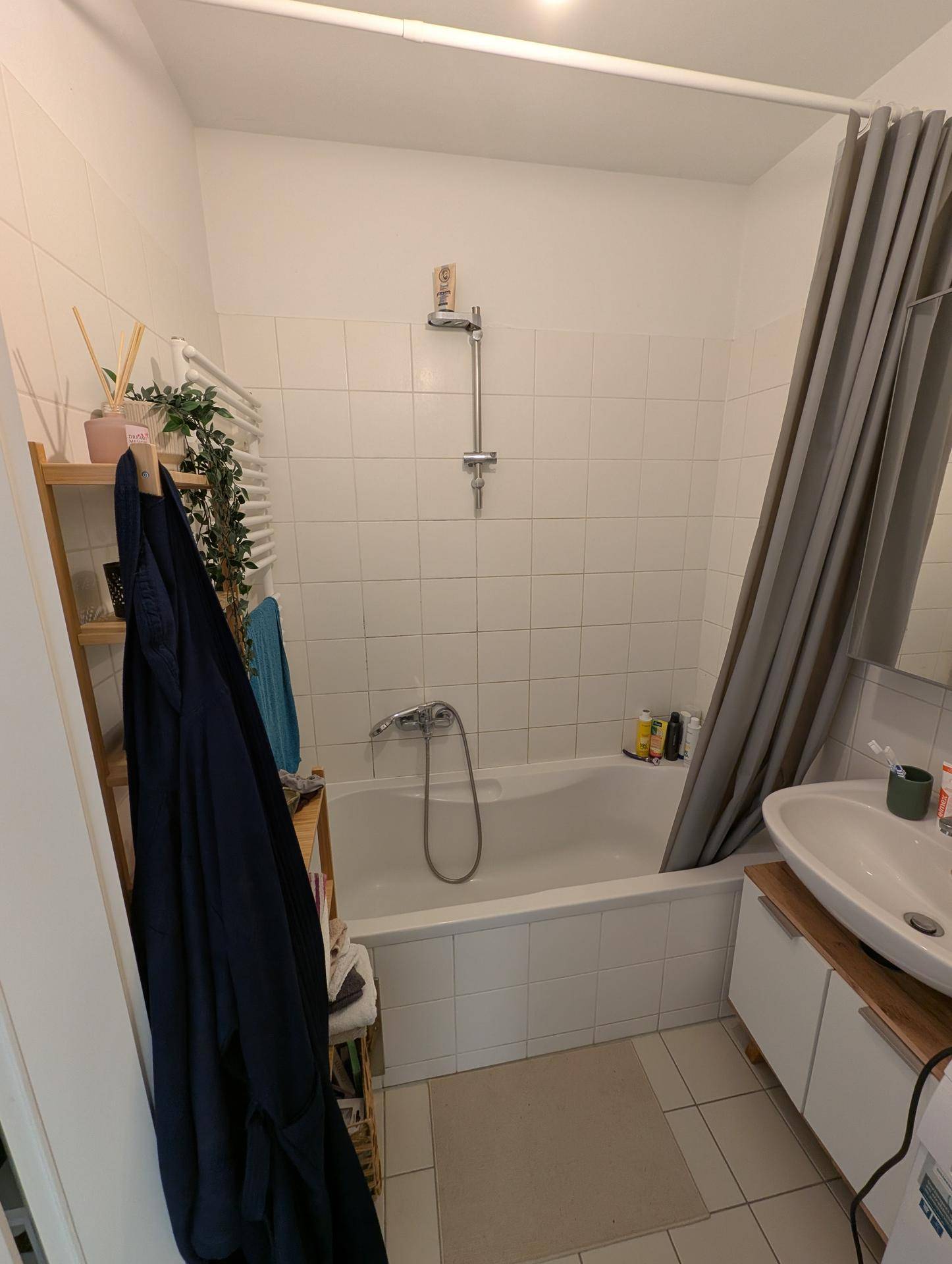 Badezimmer mit Badewanne, Duschvorhang und Waschbeckenunterschrank, weiß gefliest.