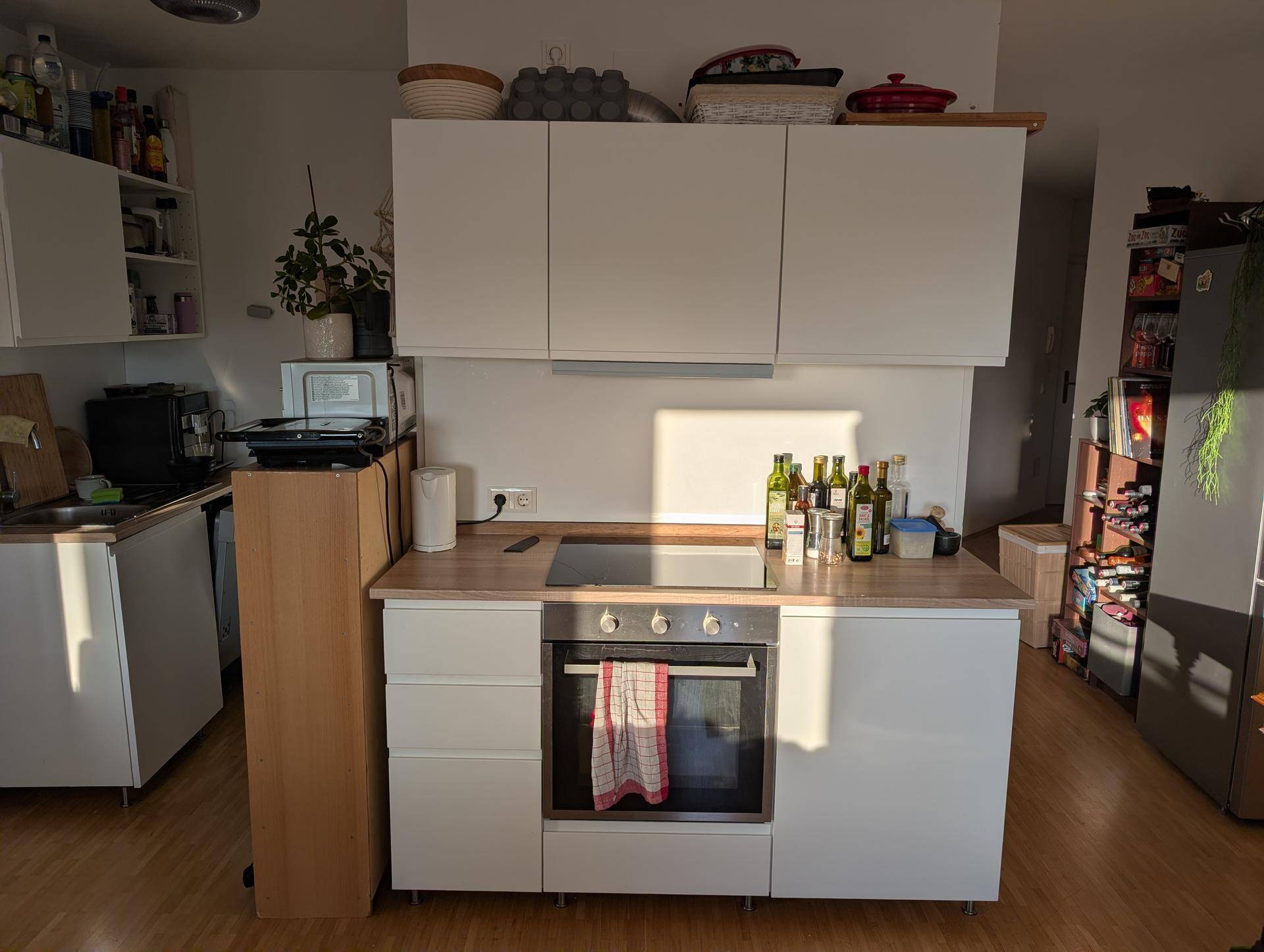 Moderne Küchenzeile mit weißen Schränken, Kochfeld und Backofen, gut beleuchtet.
