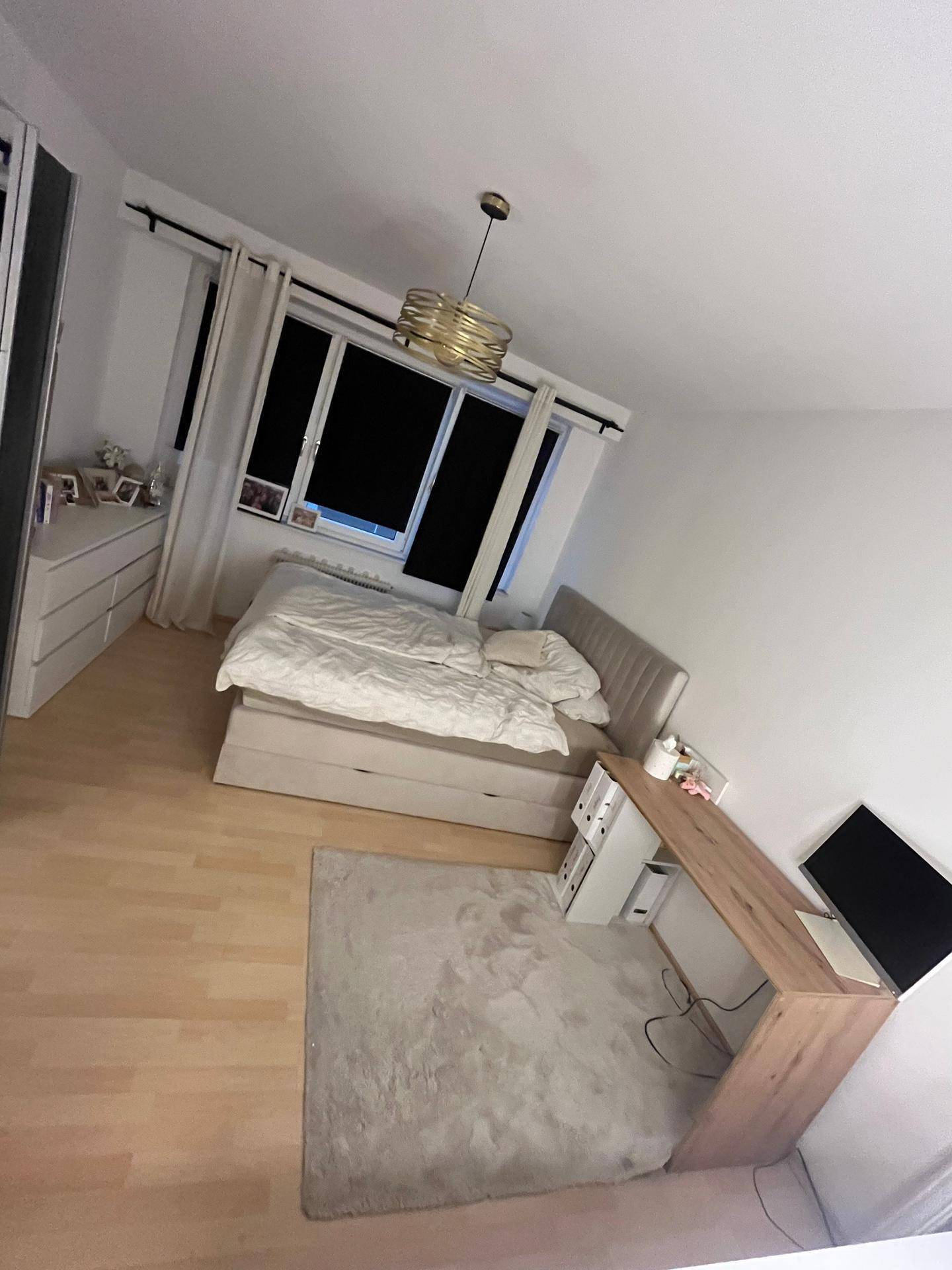 Schlafzimmer mit Bett, Kommode, Schreibtisch und moderner Deckenleuchte.