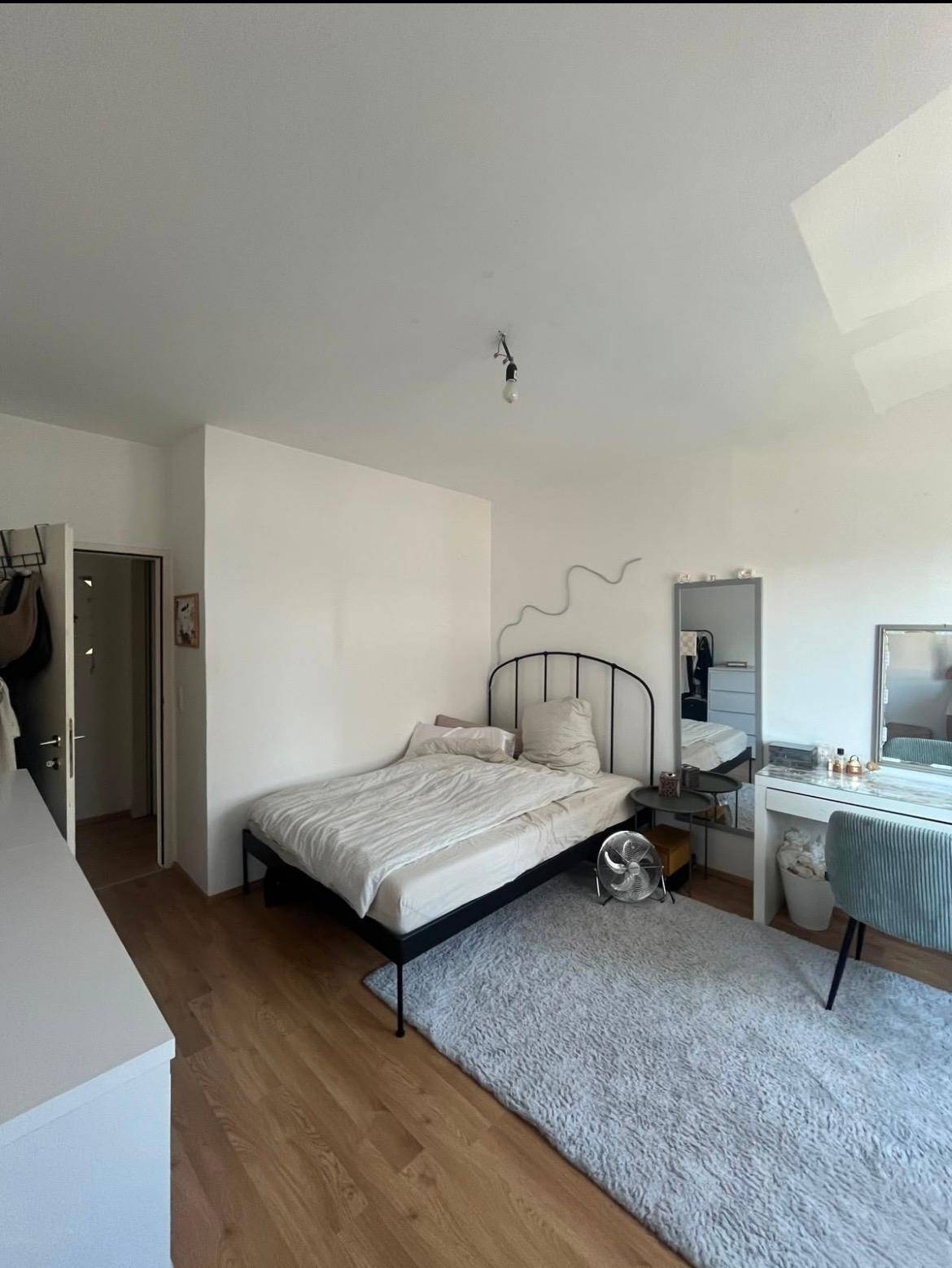 Schlafzimmer mit schwarzem Bettrahmen, hellem Teppich und Schminktisch.