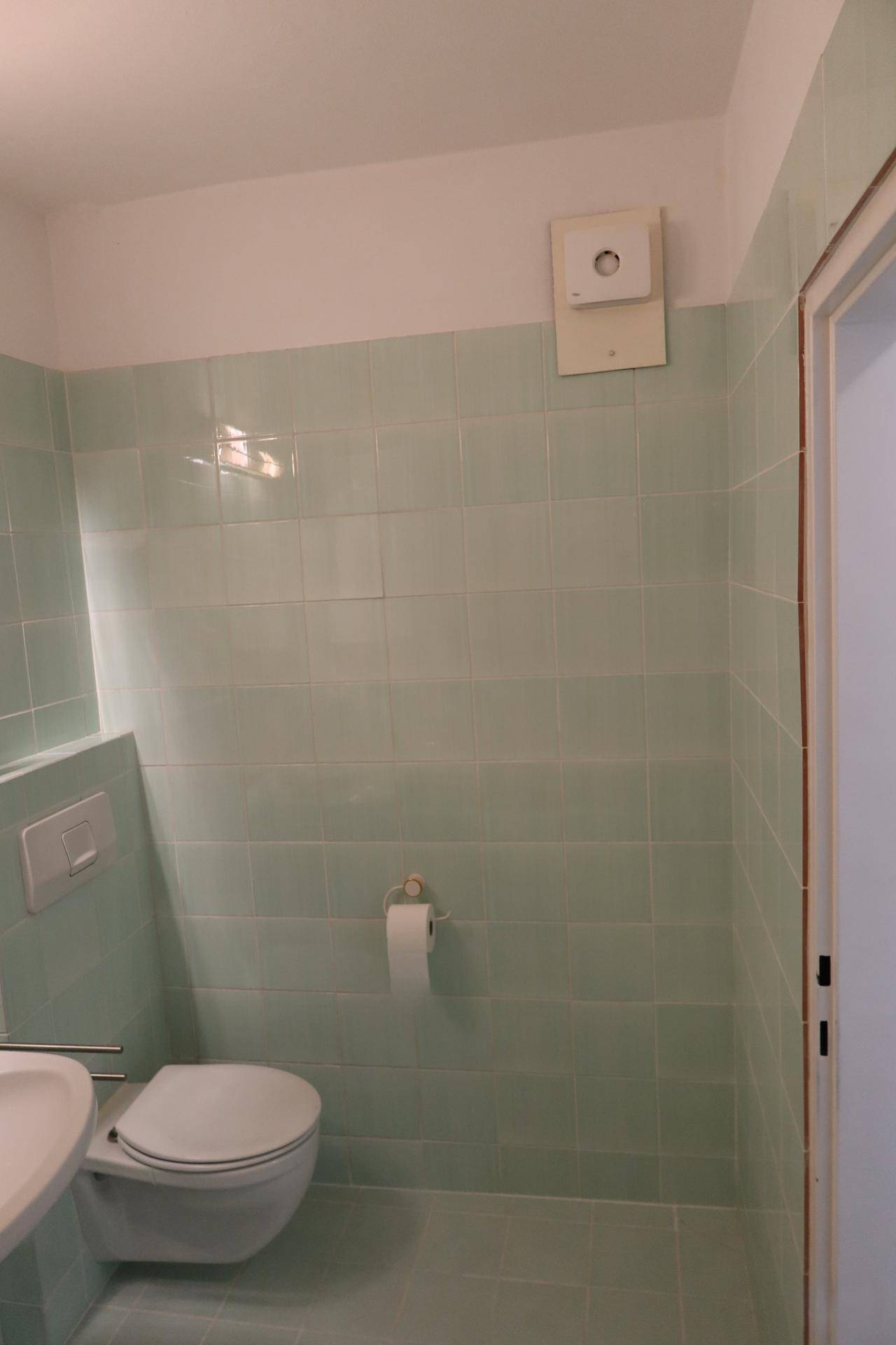 Separate Toilette mit Wand-WC, Waschbecken und hellgrünen Fliesen.
