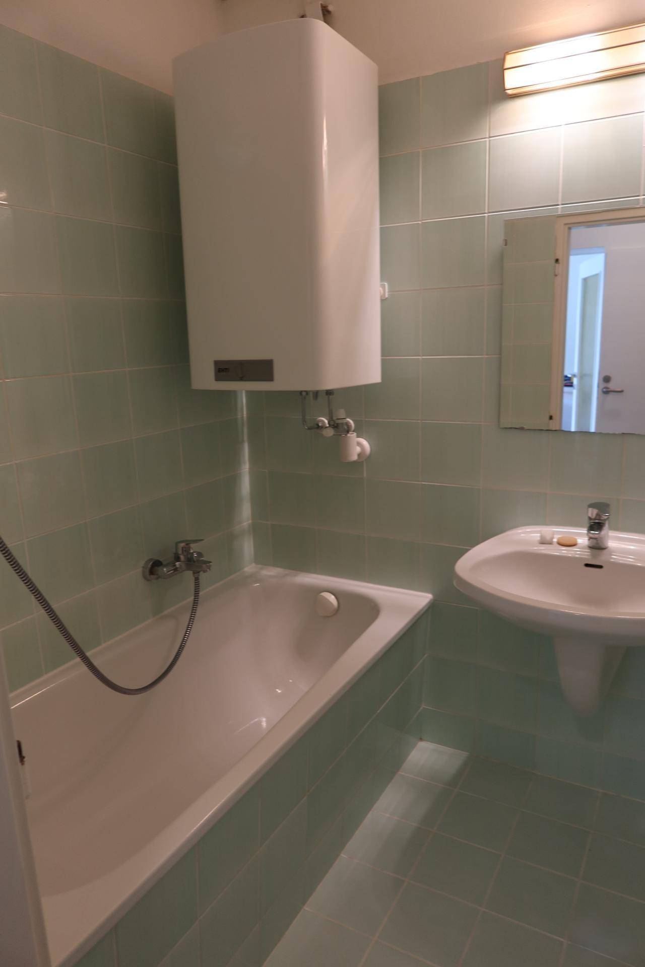 Badezimmer mit Badewanne, Waschbecken und hellgrünen Fliesen im 80er-Jahre-Stil.