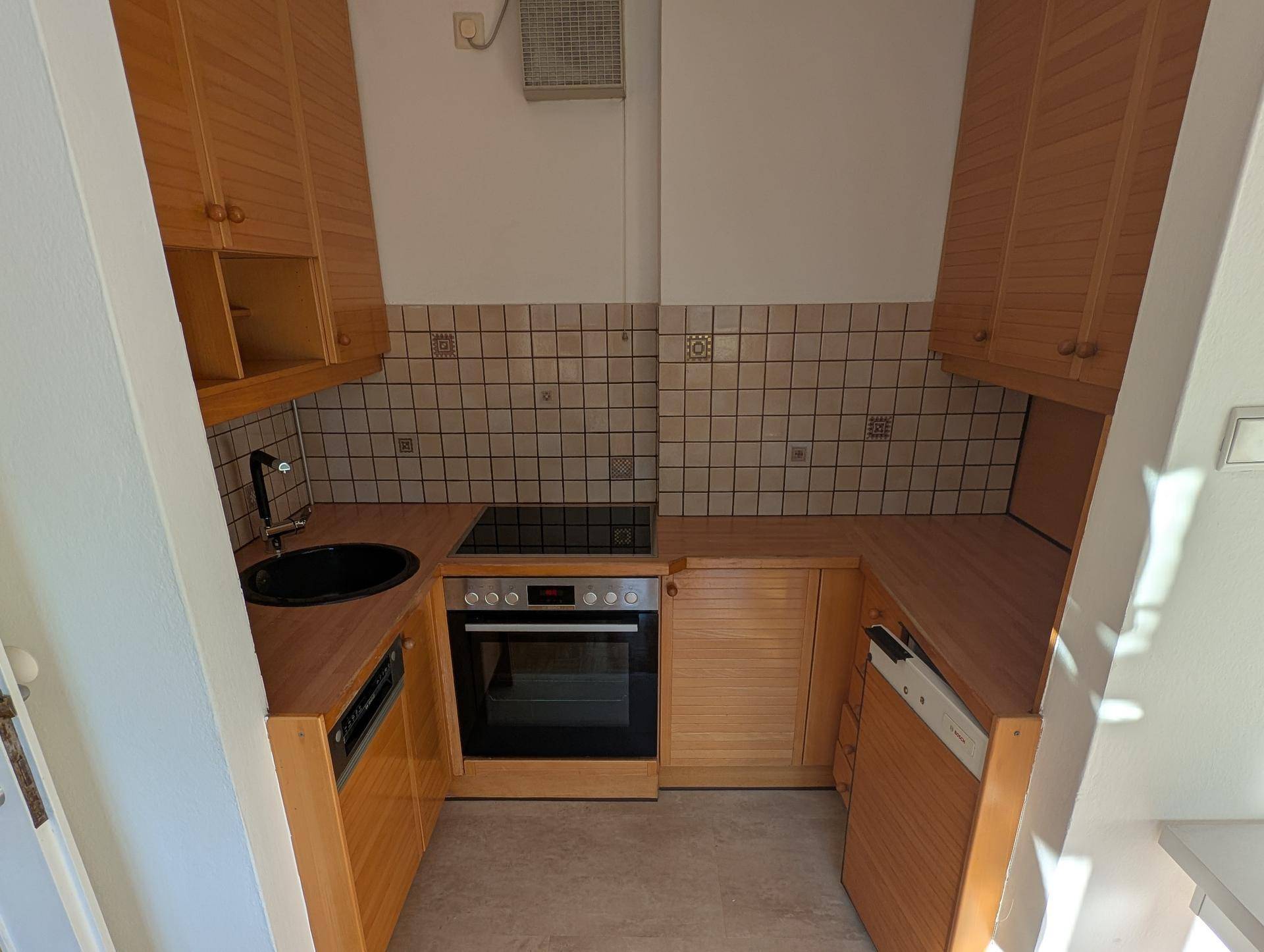 Kleine Küche mit Holzschränken, Einbaugeräten und Fliesenrückwand.